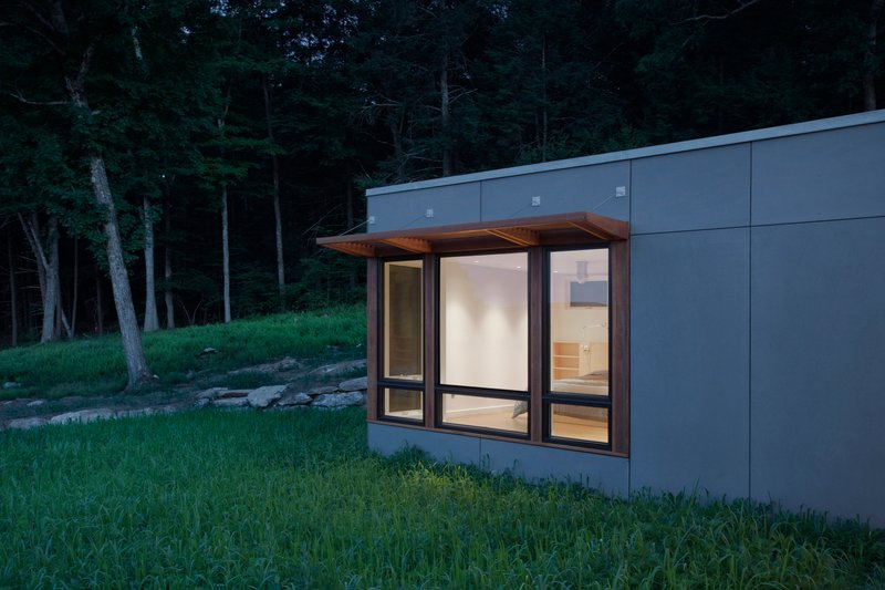 Corner bay window with timber soffit protruding from grey panel wall near wooded slope