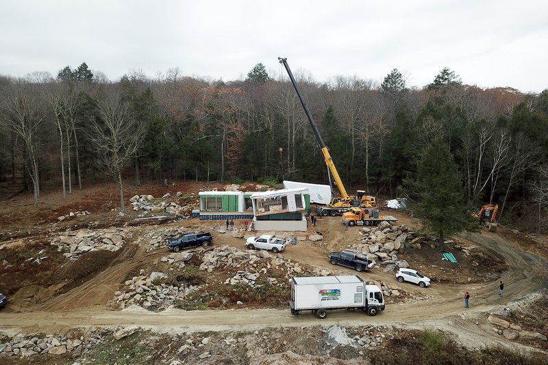 Construction site with crane lifting prefabricated modules onto cleared hillside among bare winter trees