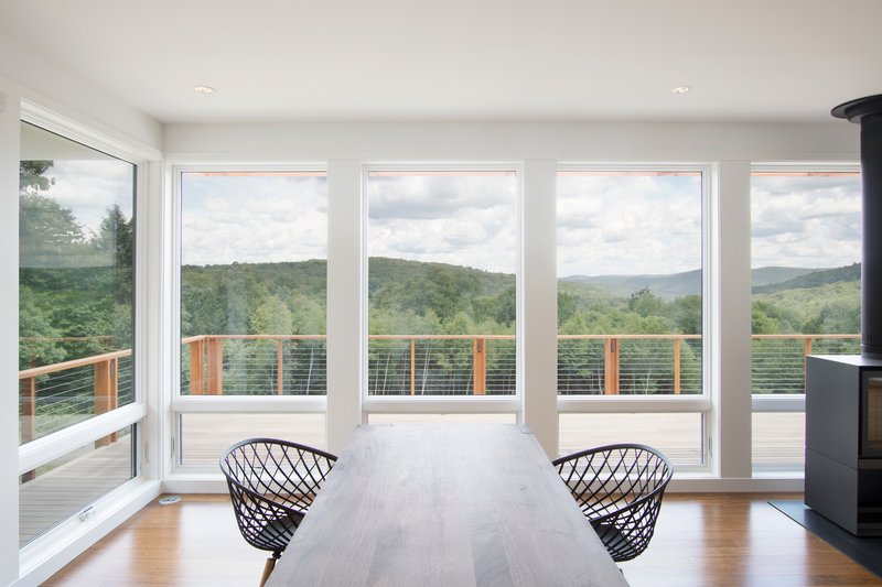 Dining area with full-height windows framing forested valley views beyond the cable railing deck