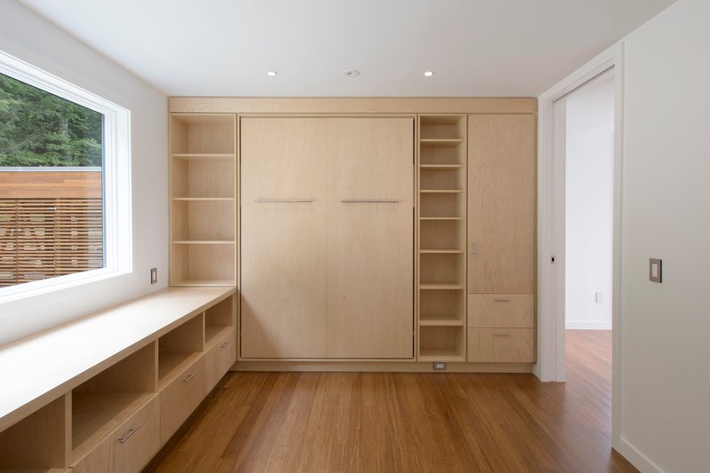 Plywood millwork wall with concealed murphy bed flanked by open shelving and window seat below deck view