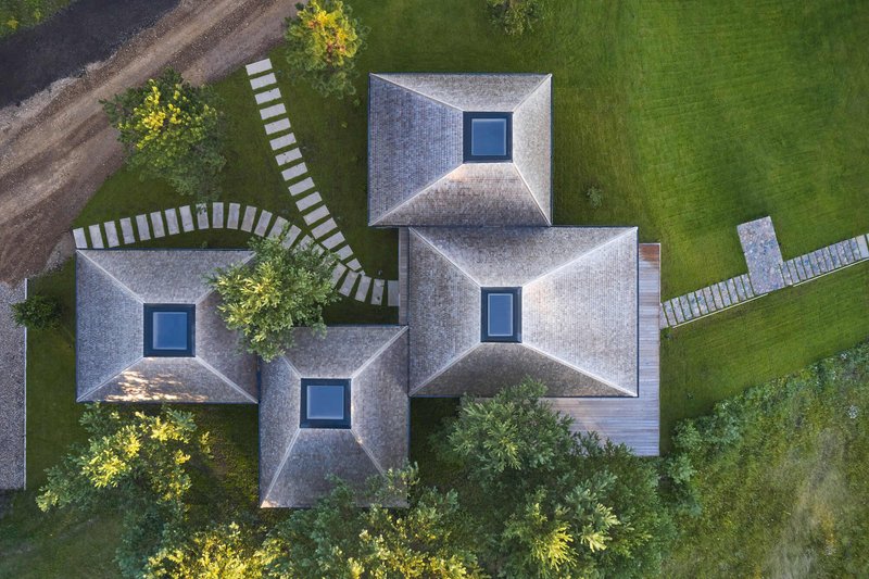 Drone view of four pyramidal shingled roofs with central skylights arranged around planted courtyards and stone pathways