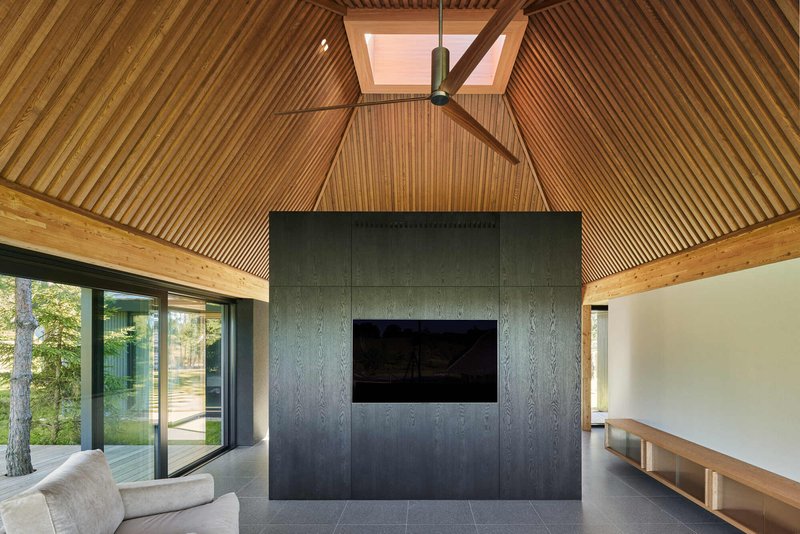 Living space with pyramidal timber slat ceiling, skylight, dark paneled fireplace core and ceiling fan