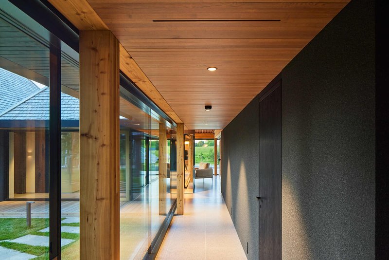 Glazed hallway with timber posts and plank ceiling looking toward another pavilion at dusk