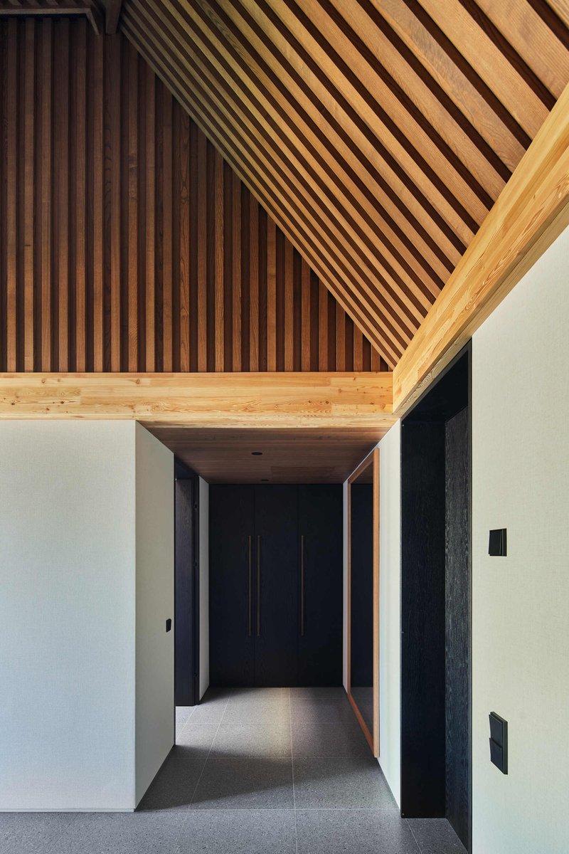 Corridor with timber slatted ceiling and dark door at the end framed by white walls