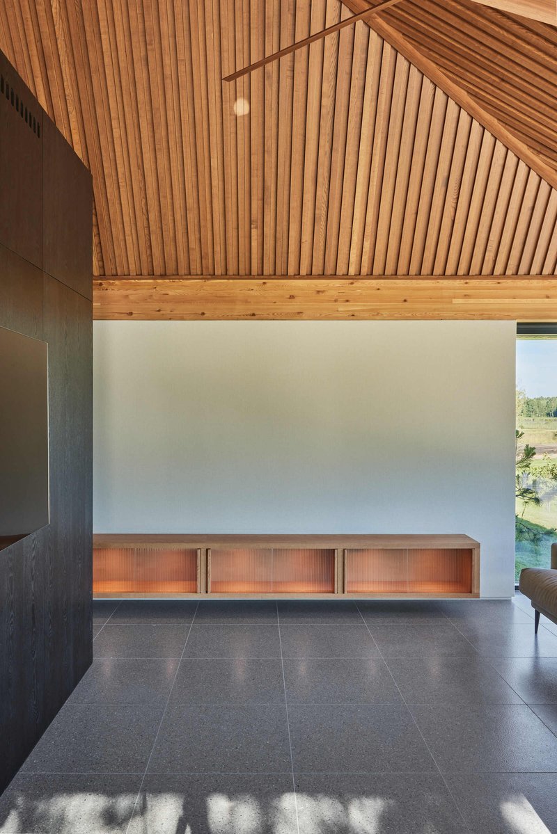 Interior with copper-lit credenza against white wall beneath angled timber slat ceiling and afternoon sun