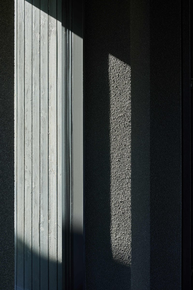 Sunlight casting sharp shadows on dark textured wall beside white vertical timber cladding