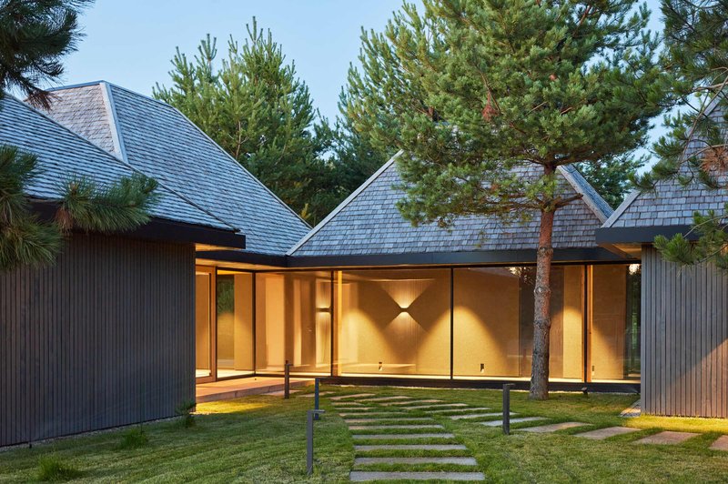 Courtyard view of illuminated pavilions with pyramidal roofs framed by pine trees at dusk