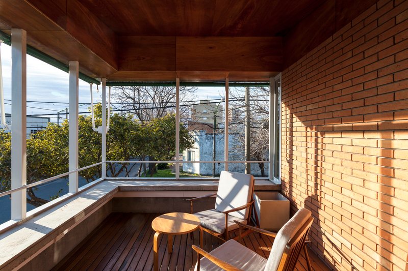 Upper-level timber-lined terrace with white steel columns, wood decking and views to neighboring rooftops in afternoon light