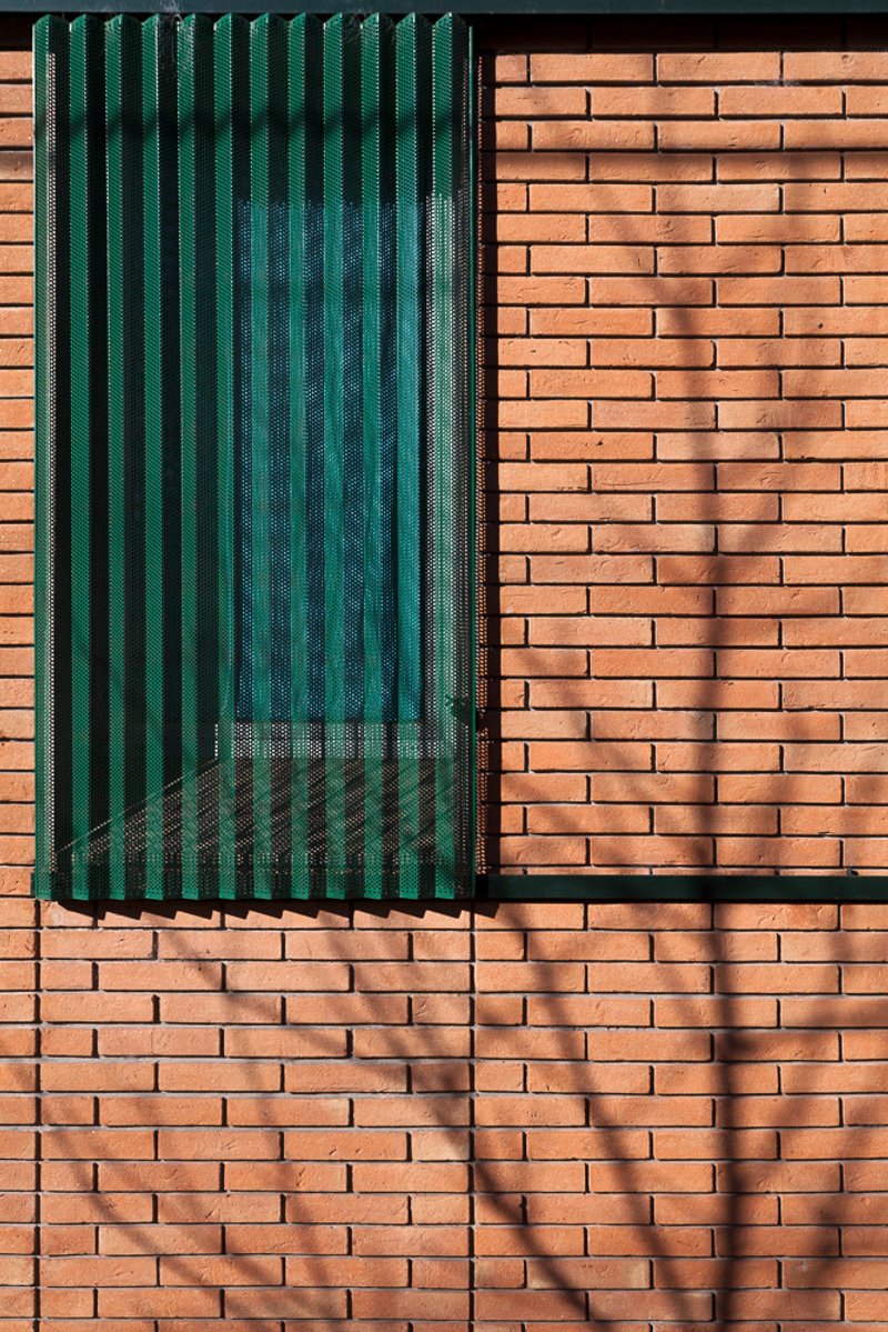 Detail of green perforated metal shutter against red brick wall with dappled shadow from nearby tree