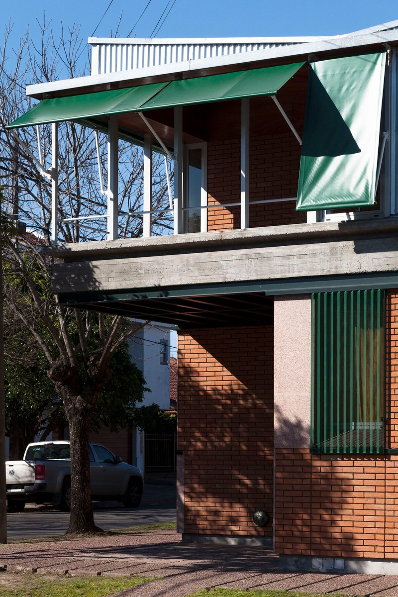 Corner view showing cantilevered concrete slab supporting the upper pavilion with white columns and hinged green awnings