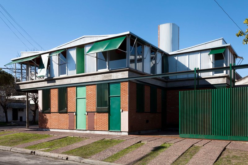 Full facade view showing brick base with green shutters below white corrugated metal upper level and central water tower