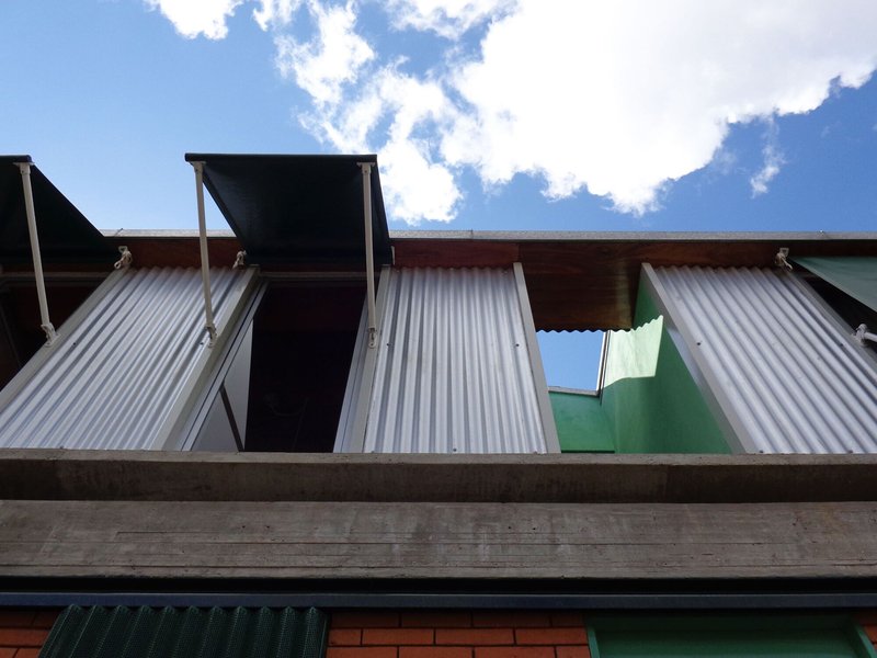 Upward view of operable corrugated metal shutters and concrete balcony edge against blue sky with white clouds