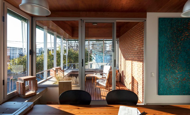 Interior dining space with timber ceiling and glazed doors opening to timber deck terrace with planted boxes