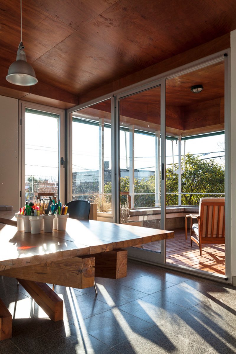 Timber dining table beneath plywood ceiling with sliding glass doors opening to timber deck and urban rooftops beyond