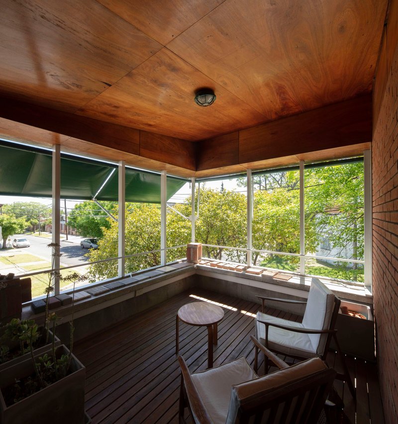 Corner window seat with plywood ceiling and walls framing views of green street trees in afternoon light