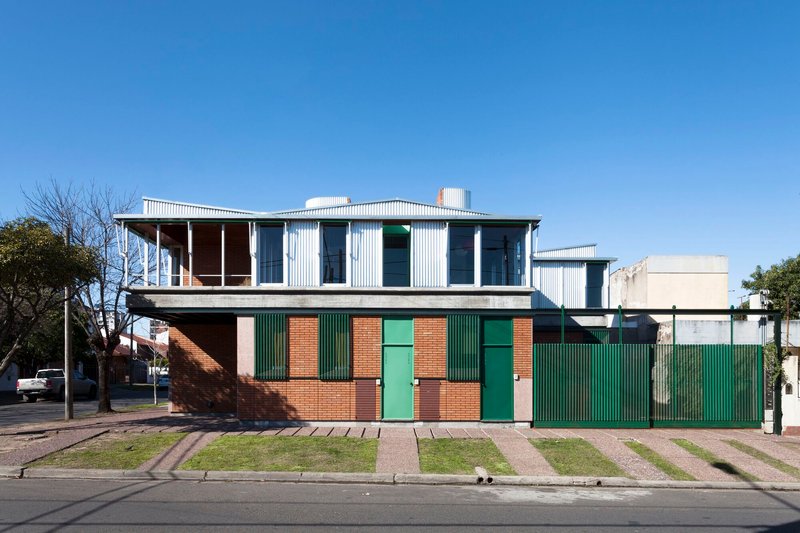 Street view of the two-story residence with red brick base, green corrugated shutters and white corrugated upper level