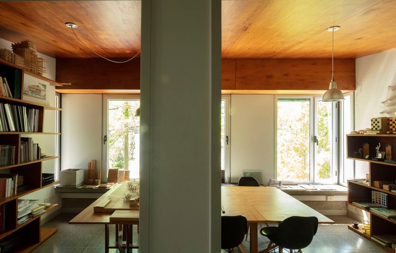 View through grey column into workspace with timber ceiling and open shelving along walls