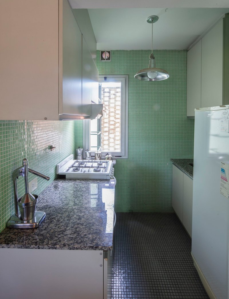 Compact kitchen with green mosaic tile walls and granite countertop under pendant light