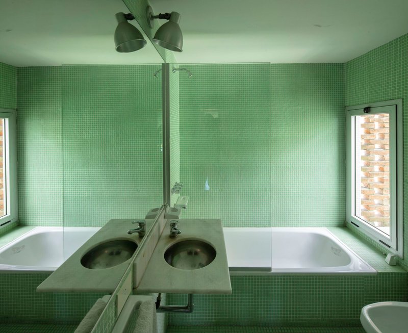 Bathroom with green mosaic tile walls, recessed tub, and dual sinks under ceiling-mounted fixture