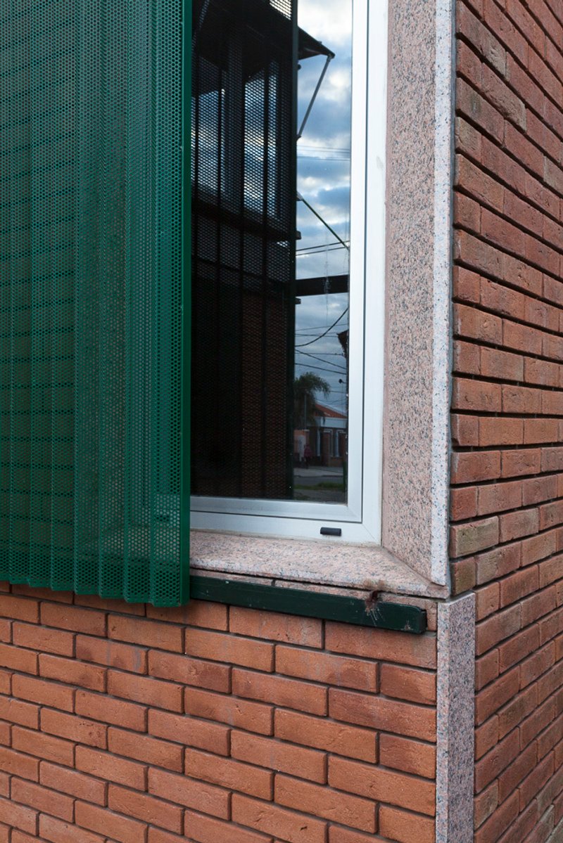 Window corner with green metal screen, granite sill and red brick wall under overcast sky