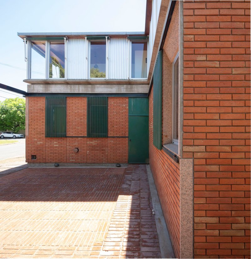 Courtyard with brick paving, red brick walls, green metal shutters and upper corrugated metal volume