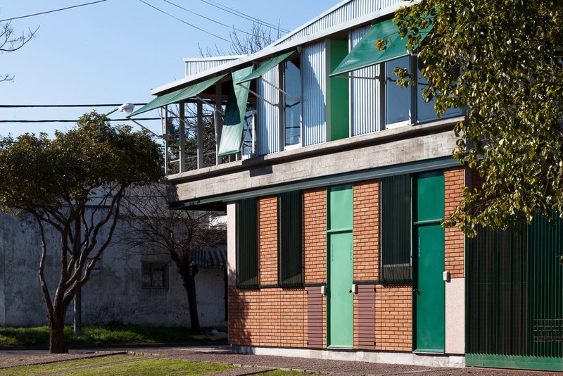 Facade showing red brick base with green metal doors and corrugated metal upper level beside bare tree