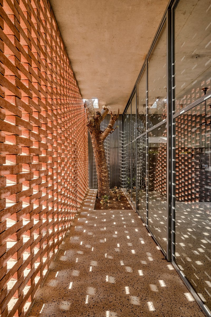 Perforated terracotta brick wall corridor casting dappled sunlight onto polished terrazzo flooring