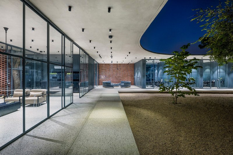 Central courtyard at dusk with gravel paths converging beneath a concrete roof and perforated brick screen wall