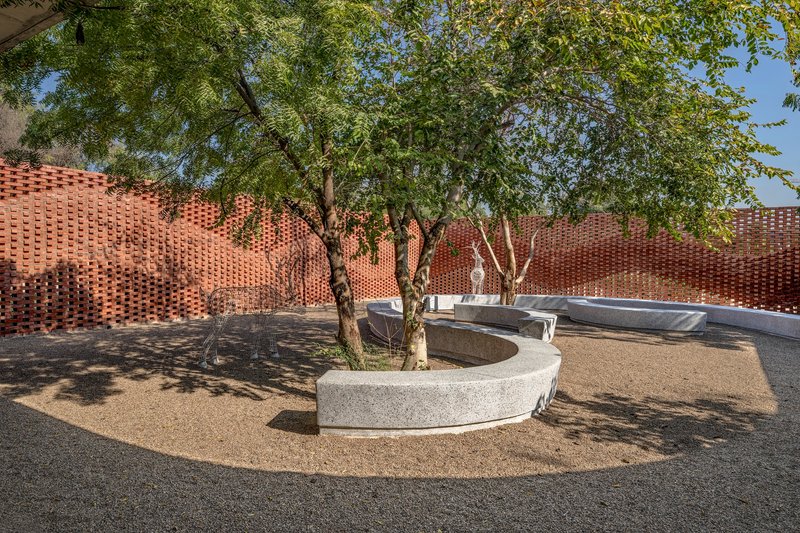 Courtyard with circular concrete planter surrounding existing trees and perforated brick wall in the background