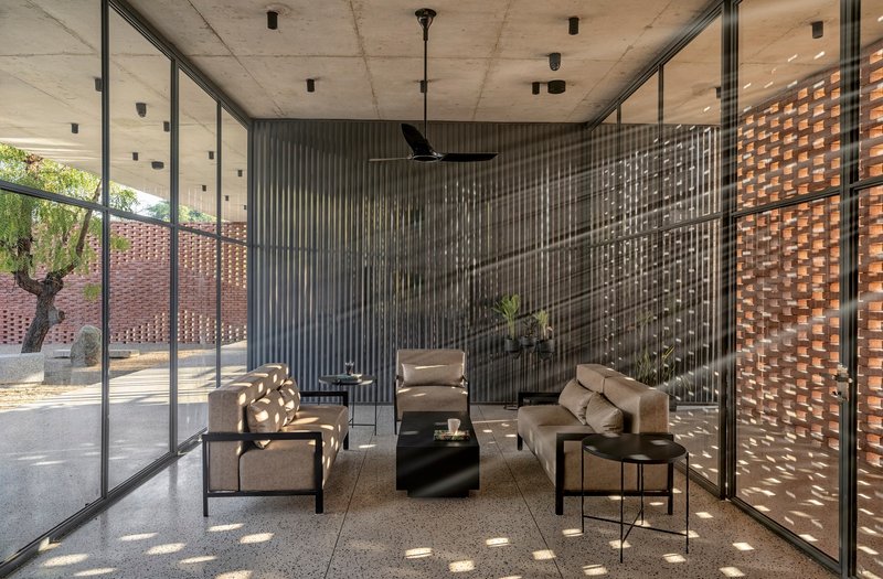 Interior living space with concrete ceiling and corrugated metal screen filtering dappled light from the courtyard