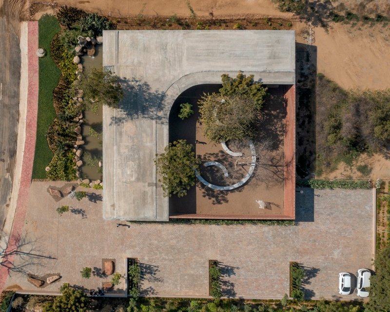 Drone view of the curved concrete roof cutout revealing the courtyard tree and circular bench below