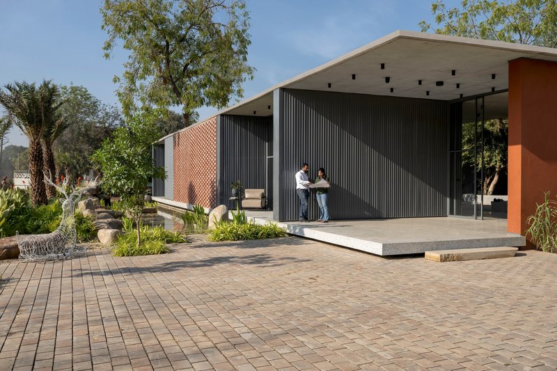 Front elevation showing perforated brick facade and corrugated metal cladding with covered terrace and brick paving