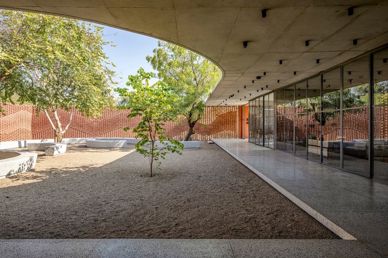 Covered courtyard beneath a curved concrete roof with glazed walls and gravel ground plane