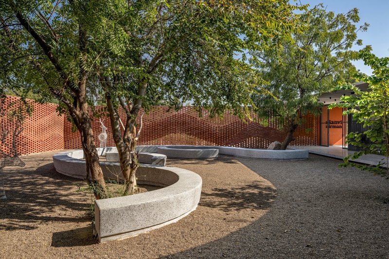 Circular tree planter in gravel courtyard framed by undulating perforated brick boundary wall