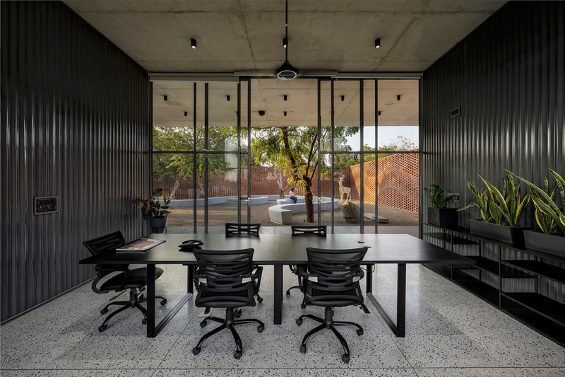 Conference room with black corrugated metal walls and floor-to-ceiling glazing opening to a courtyard with trees