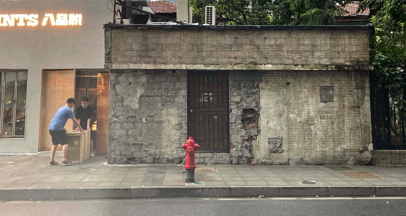 Weathered concrete structure with boarded windows and red fire hydrant on sidewalk