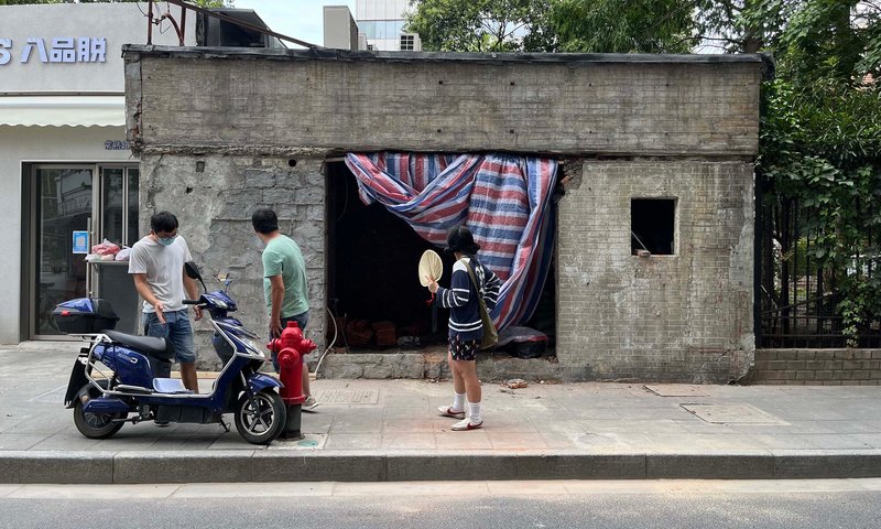 Derelict concrete building with striped curtain covering opening and pedestrians gathering on the street
