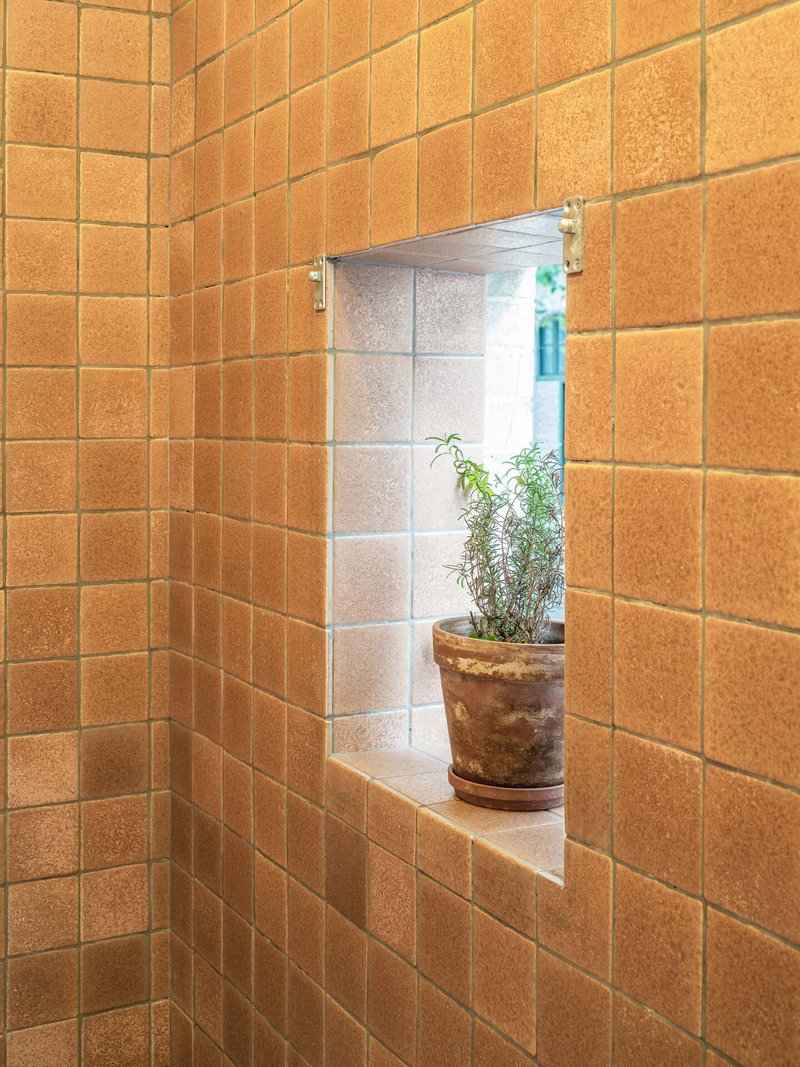 Corner niche framed in orange glazed tile wall with a potted plant on the ledge