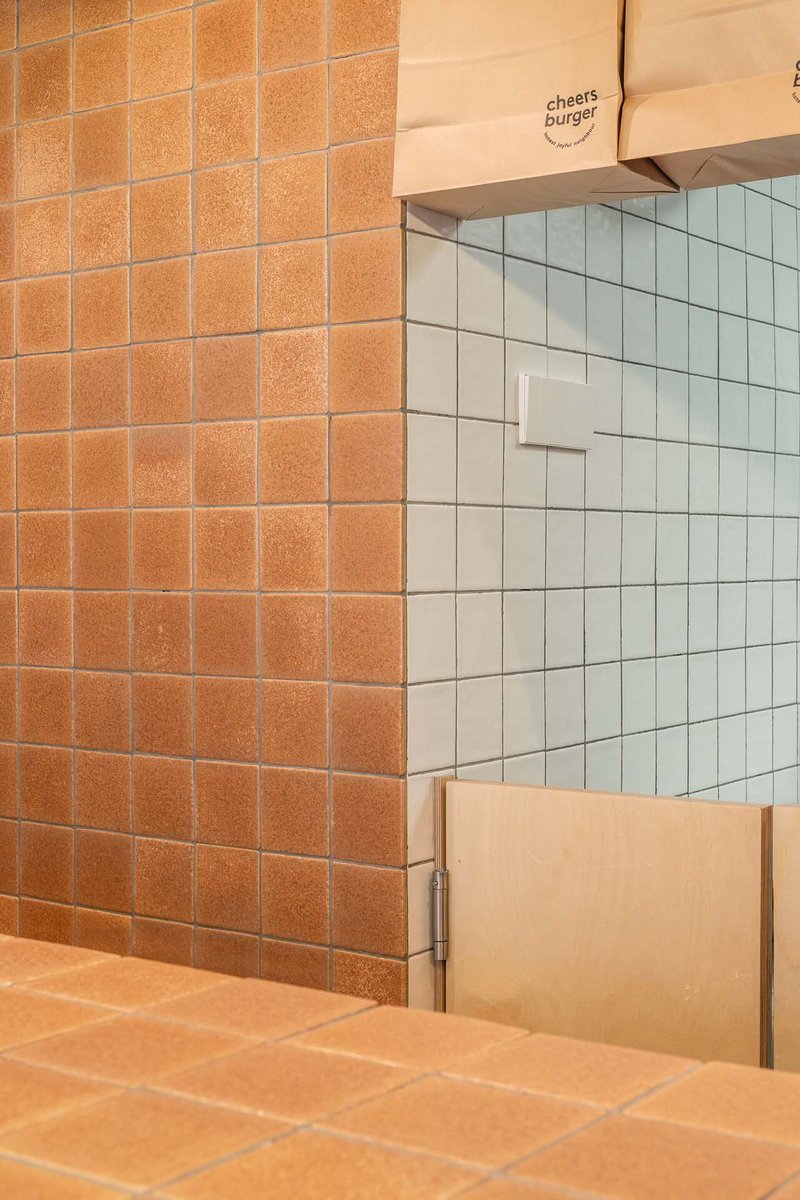 Junction of orange and pale green tiled walls with recessed white paper towel dispenser
