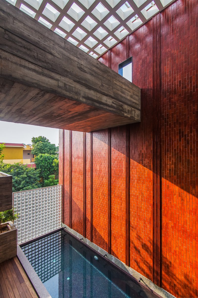 Cantilevered concrete balcony above a courtyard pool with red terracotta tile wall and gridded skylight