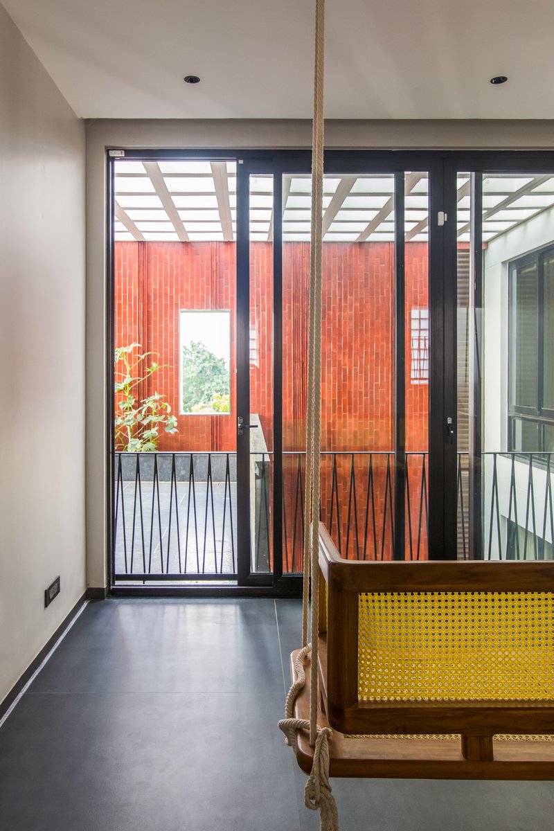Interior corridor with rope swing and glazed doors opening to terracotta-clad courtyard under pergola