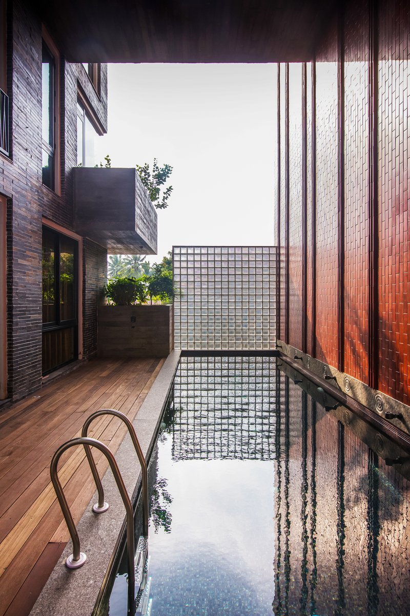 Narrow courtyard pool with timber deck and glass block wall under an open sky