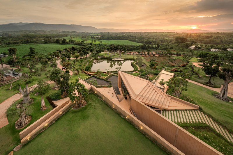 Aerial view of the angular folded roof planes rising above manicured lawns and a pond at sunset