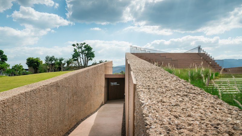 Passage between textured stone walls leading to a recessed entrance under a planted green roof