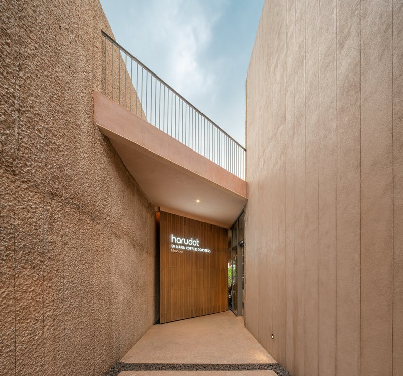 Entry passage between textured wall and smooth vertical panels beneath a cantilevered overhang with metal railing