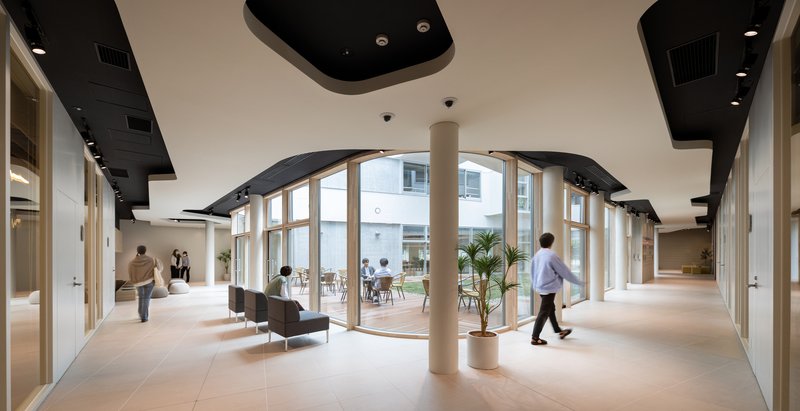 Interior corridor with curved glazed wall, black ceiling panels and cylindrical column as people walk through