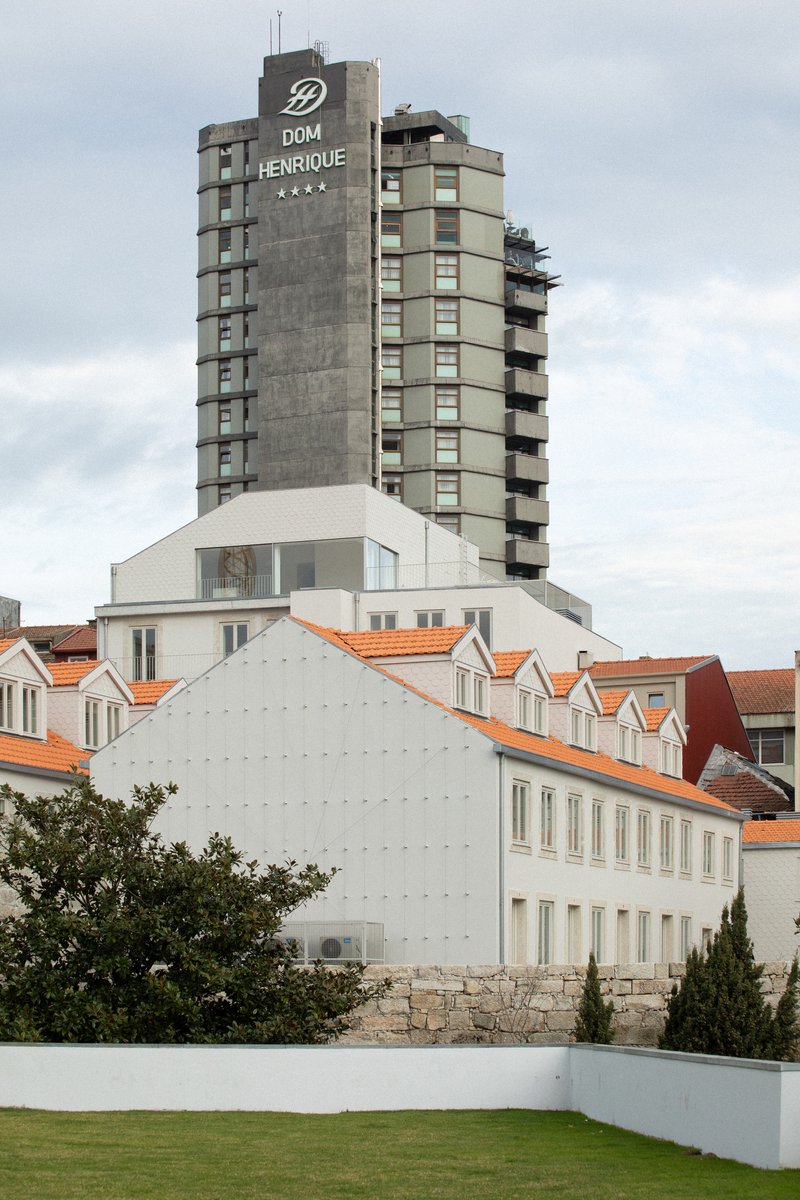 White gable facade and orange-tiled roofline beneath a concrete high-rise tower under cloudy skies