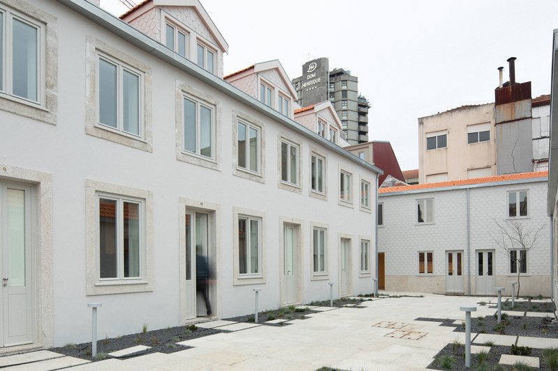 Paved courtyard between white-rendered residential facades with scattered planting beds and young saplings