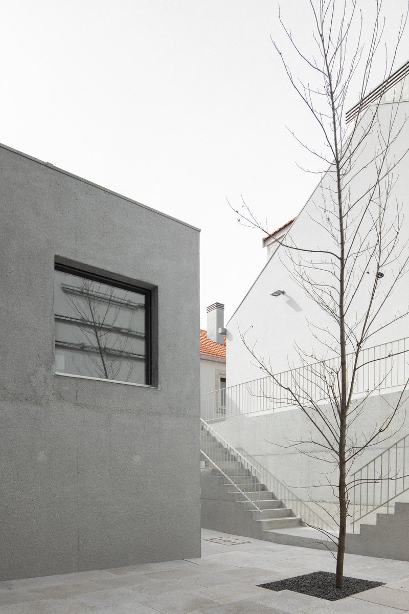 Courtyard view showing a grey rendered wall with square window and bare tree beside an exterior staircase