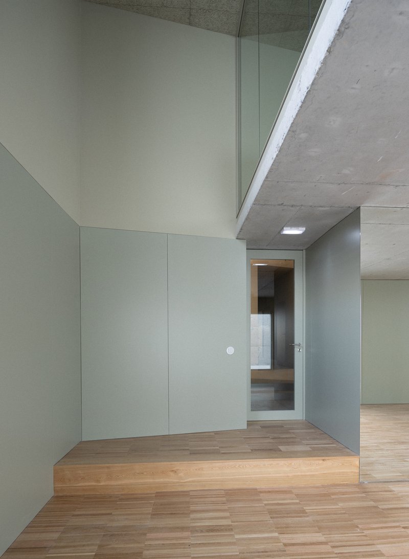 Interior corner with pale grey panels and wood flooring under a skylit concrete soffit